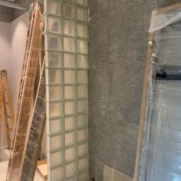 Majessbud Sp. z o.o. - Ściana z luksferów w trakcie montażu, widoczne drewniane podpory i fragment surowej ściany o szorstkiej fakturze.