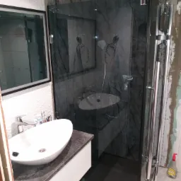 Łazienka w trakcie prac w Nowogardzie: widoczna umywalka nablatowa na szafce, kabina prysznicowa z deszczownicą oraz fragment ściany w trakcie wykańczania.