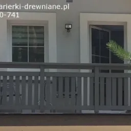 Szara, drewniana balustrada balkonowa z pionowymi szczeblami na tle jasnej elewacji z dwoma oknami, z których jedno jest otwarte.