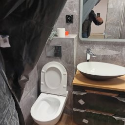 Galaxy - Łazienka w trakcie zabezpieczania przed pracami wykończeniowymi, widoczna toaleta, umywalka nablatowa i lustro, wszystko osłonięte folią malarską.