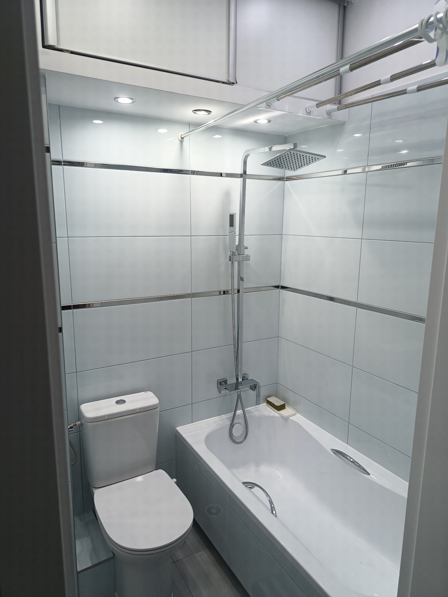 Jasna łazienka z białą armaturą, kabiną prysznicową z deszczownicą, toaletą i płytkami z metalowymi listwami dekoracyjnymi.