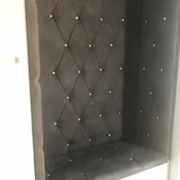 Wnęka z siedziskiem obita ciemnoszarym welurem w romby, zdobiona kryształkami, wbudowana w białą szafę.