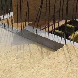 Zorza-Budownictwo - Szare, betonowe wzmocnienie z wystającymi prętami zbrojeniowymi, widoczne na tle drewnianego szalunku i żółtych elementów konstrukcyjnych.