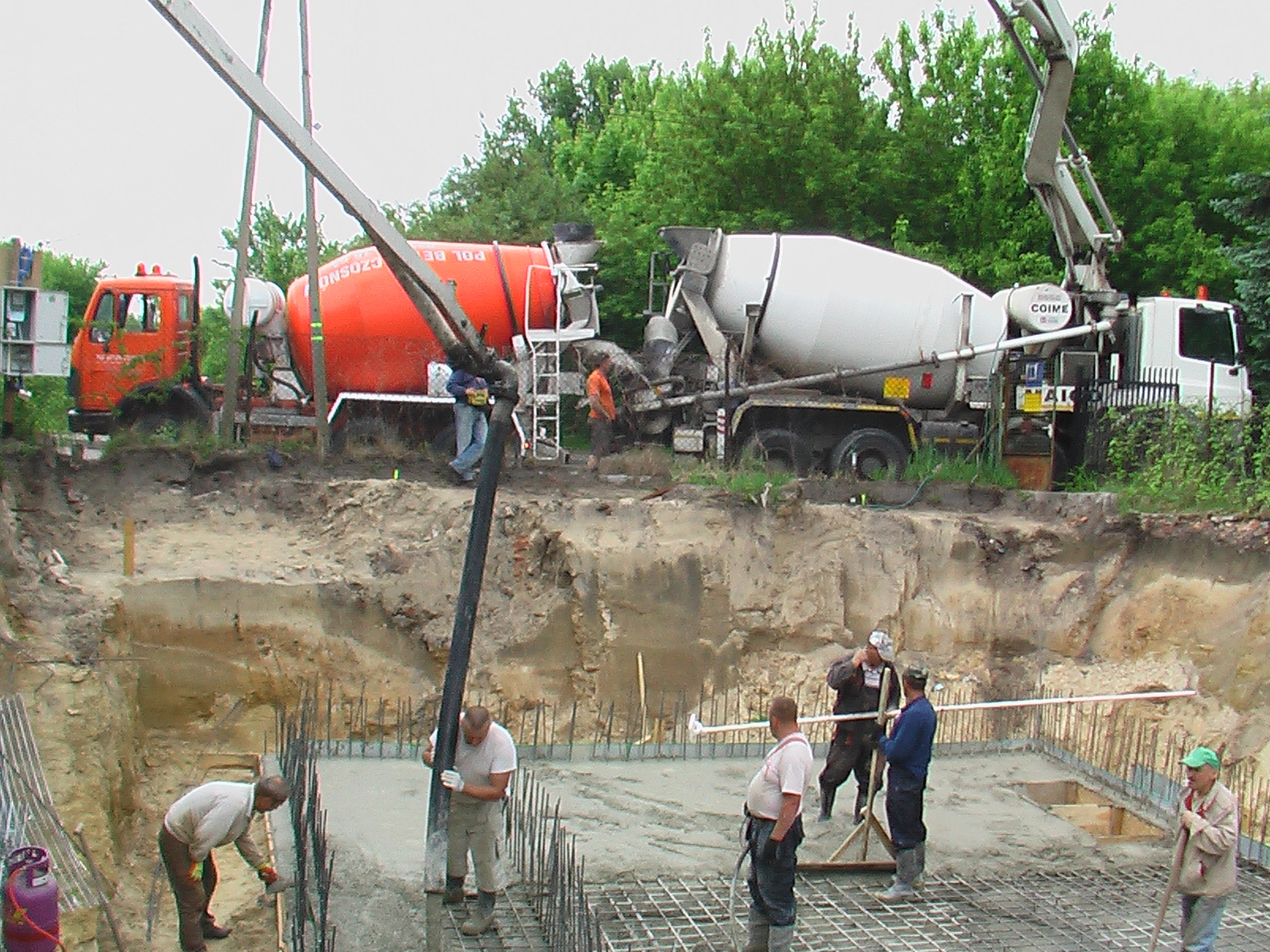 Wylewanie fundamentów budynku wielomieszkaniowego w Warszawie, widoczne betoniarki i pracownicy podczas betonowania zbrojenia.