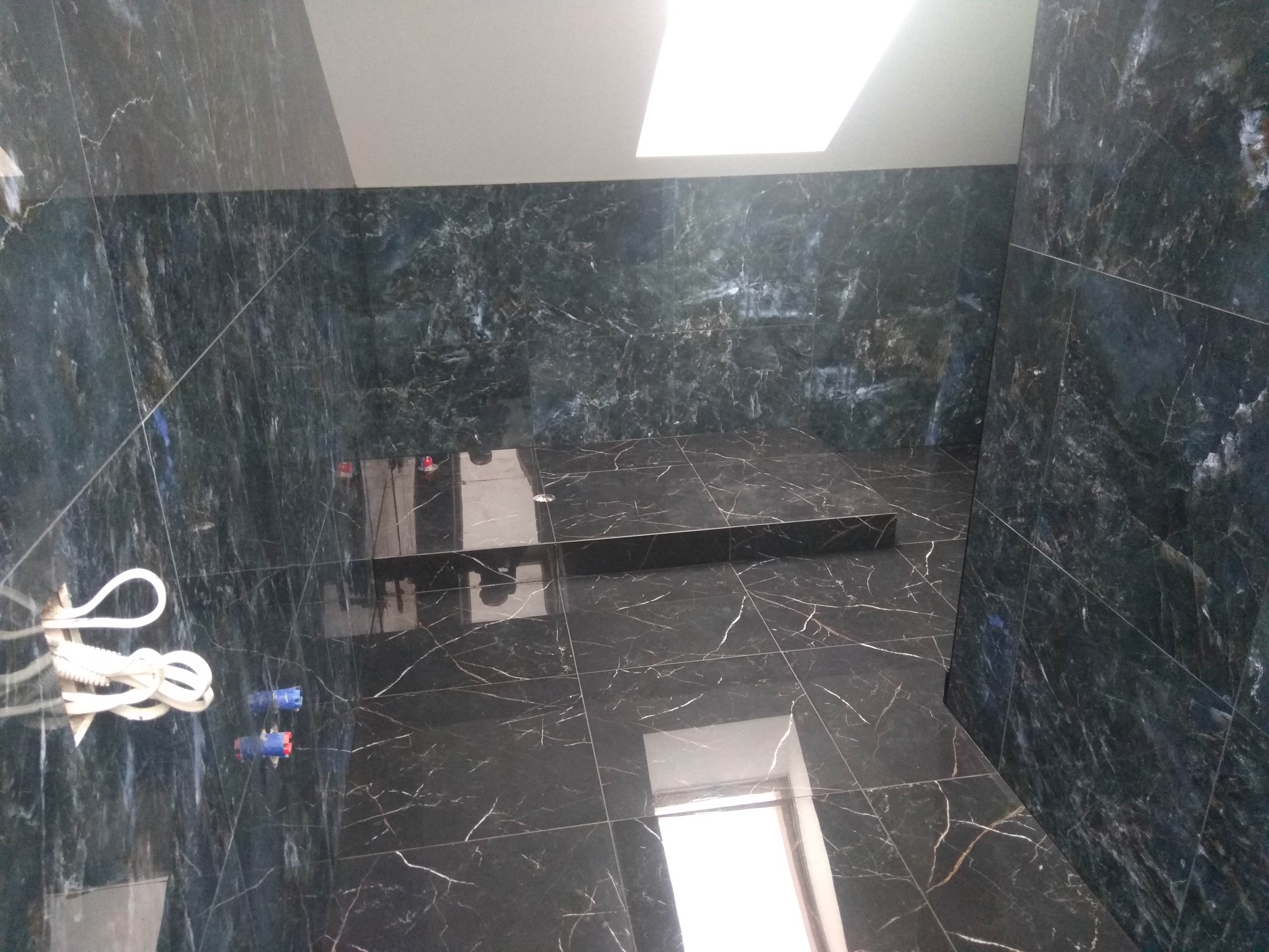 Wykończona łazienka z ciemnymi, marmurkowymi płytkami, widoczne przewody wystające ze ściany, okno w dolnej części kadru.