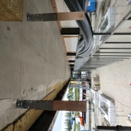 Widok z góry na fragment budynku w trakcie ocieplania, widoczne płyty izolacyjne, metalowe mocowania i drewniane elementy konstrukcyjne.