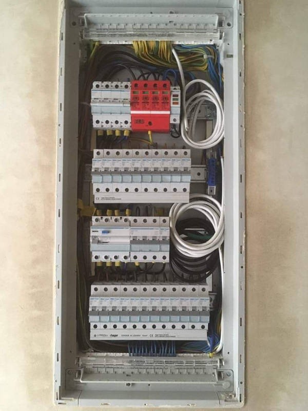 Wnętrze skrzynki elektrycznej z zainstalowanymi bezpiecznikami, przewodami i zabezpieczeniami, widoczne różnokolorowe kable i elementy montażowe.