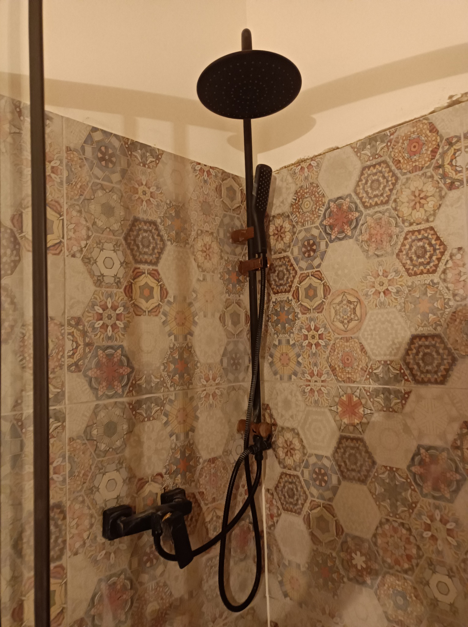 Czarny zestaw prysznicowy z deszczownicą i słuchawką na tle ściany wyłożonej heksagonalnymi płytkami w stylu patchwork.