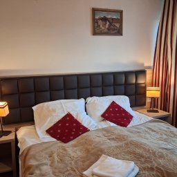 PP DP DMYTRO PYROHOV - Pokój hotelowy z łóżkiem małżeńskim, lampkami nocnymi i obrazem na ścianie. Beżowa narzuta z wytłaczanym wzorem. Czerwone poduszki dekoracyjne.