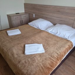 PP DP DMYTRO PYROHOV - Pokój hotelowy z brązową narzutą w kwiaty, dwoma białymi poduszkami i ręcznikami. Widoczna szafka nocna i drewniane wykończenie ściany za łóżkiem.