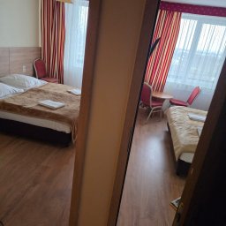 PP DP DMYTRO PYROHOV - Pokój hotelowy z dwoma łóżkami, stolikiem i krzesłami, widziany z perspektywy drzwi. Czerwono-białe zasłony i drewniana podłoga dodają ciepła wnętrzu.