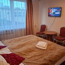 PP DP DMYTRO PYROHOV - Pokój hotelowy w Gdańsku z beżową narzutą na łóżku, czerwonymi poduszkami, telewizorem Smart TV na ścianie i dwoma krzesłami przy okrągłym stoliku.