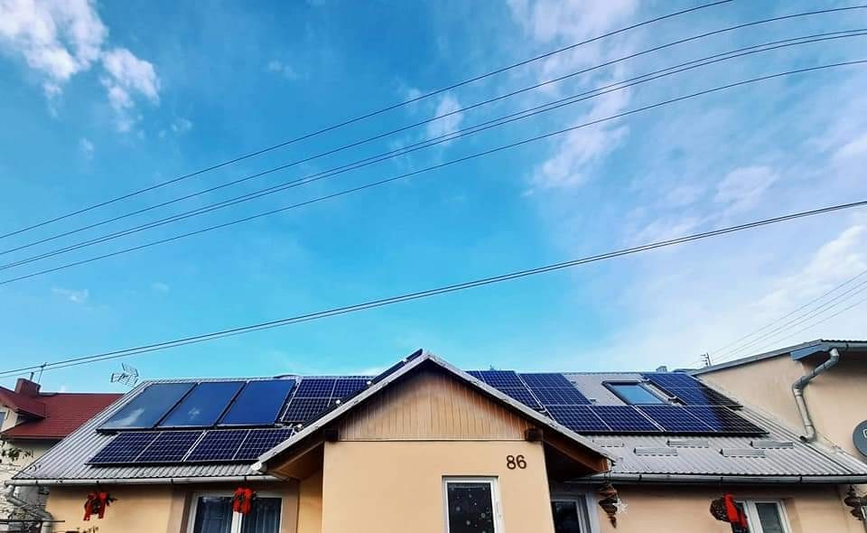 Dom jednorodzinny z panelami słonecznymi na dachu, widok na błękitne niebo z liniami energetycznymi, numer domu 86.