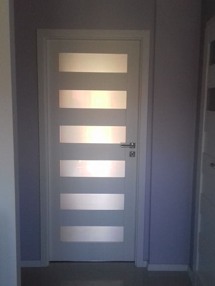 Szare drzwi wewnętrzne z poziomymi, matowymi przeszkleniami w pomalowanym na fioletowo pomieszczeniu.