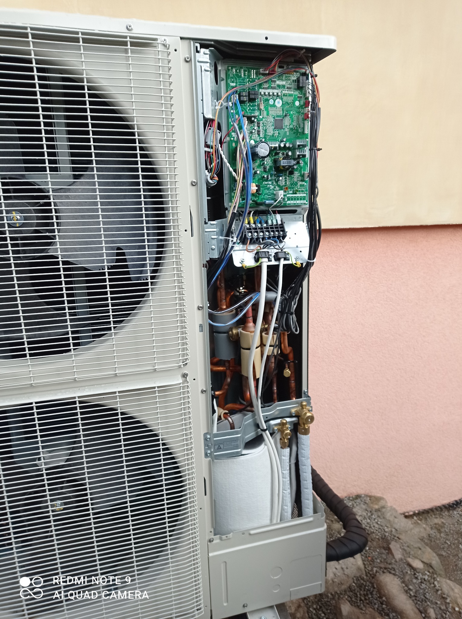 Otwarta obudowa zewnętrznej jednostki pompy ciepła, widoczne miedziane rury, elektronika i wentylator.