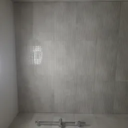 Szara łazienka z pionowymi żłobieniami na ścianach, chromowana bateria prysznicowa na podłodze i okrągła lampa sufitowa LED