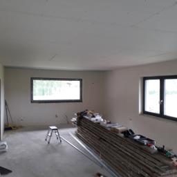 Mar-Wik - Wnętrze w trakcie prac wykończeniowych: surowy beton na podłodze, ściany przygotowane do malowania, widoczne profile aluminiowe, deski i narzędzia, sufit częściowo wykończony z widocznymi punktami...