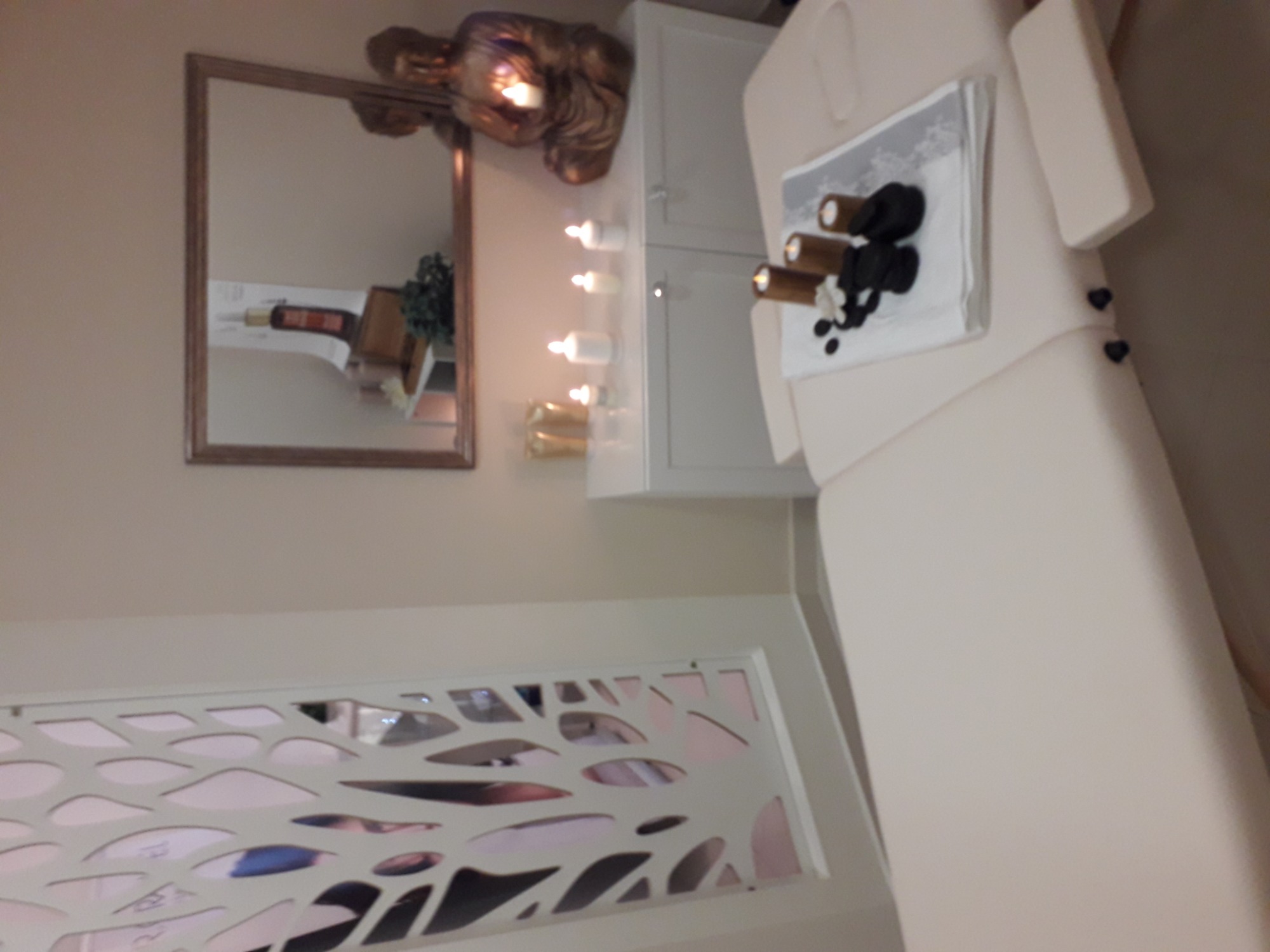 Jasny gabinet kosmetyczny z leżanką, dekoracyjnym panelem ściennym, lustrem i świecami.