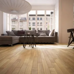 Jasna drewniana podłoga parkietowa w nowoczesnym salonie z szarym narożnikiem, stolikiem kawowym i dużym oknem z widokiem na budynki.