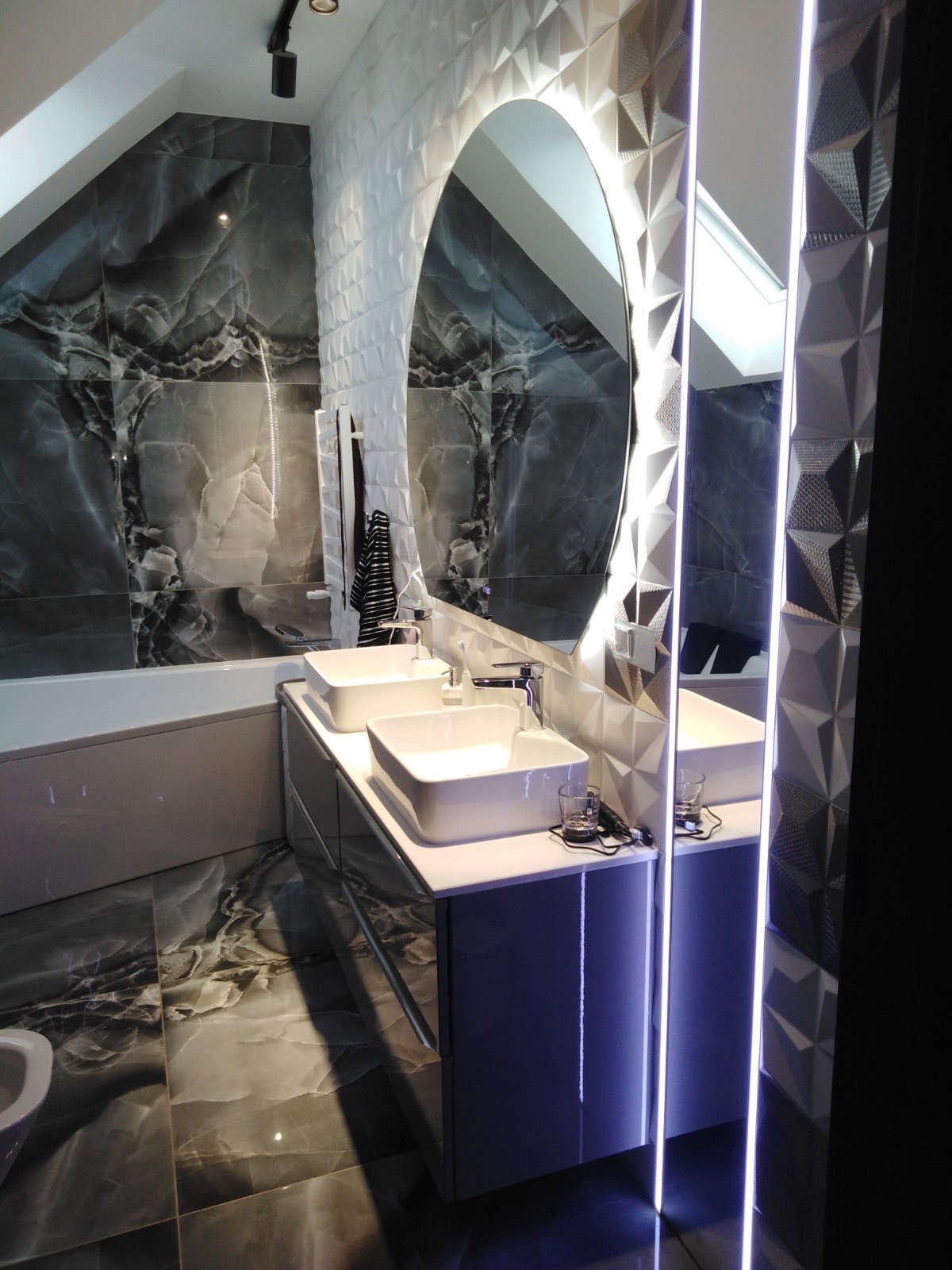 Nowoczesna łazienka w Szczecinie na poddaszu z dwoma białymi umywalkami nablatowymi, podświetlanym okrągłym lustrem i płytkami imitującymi marmur na ścianach i podłodze.