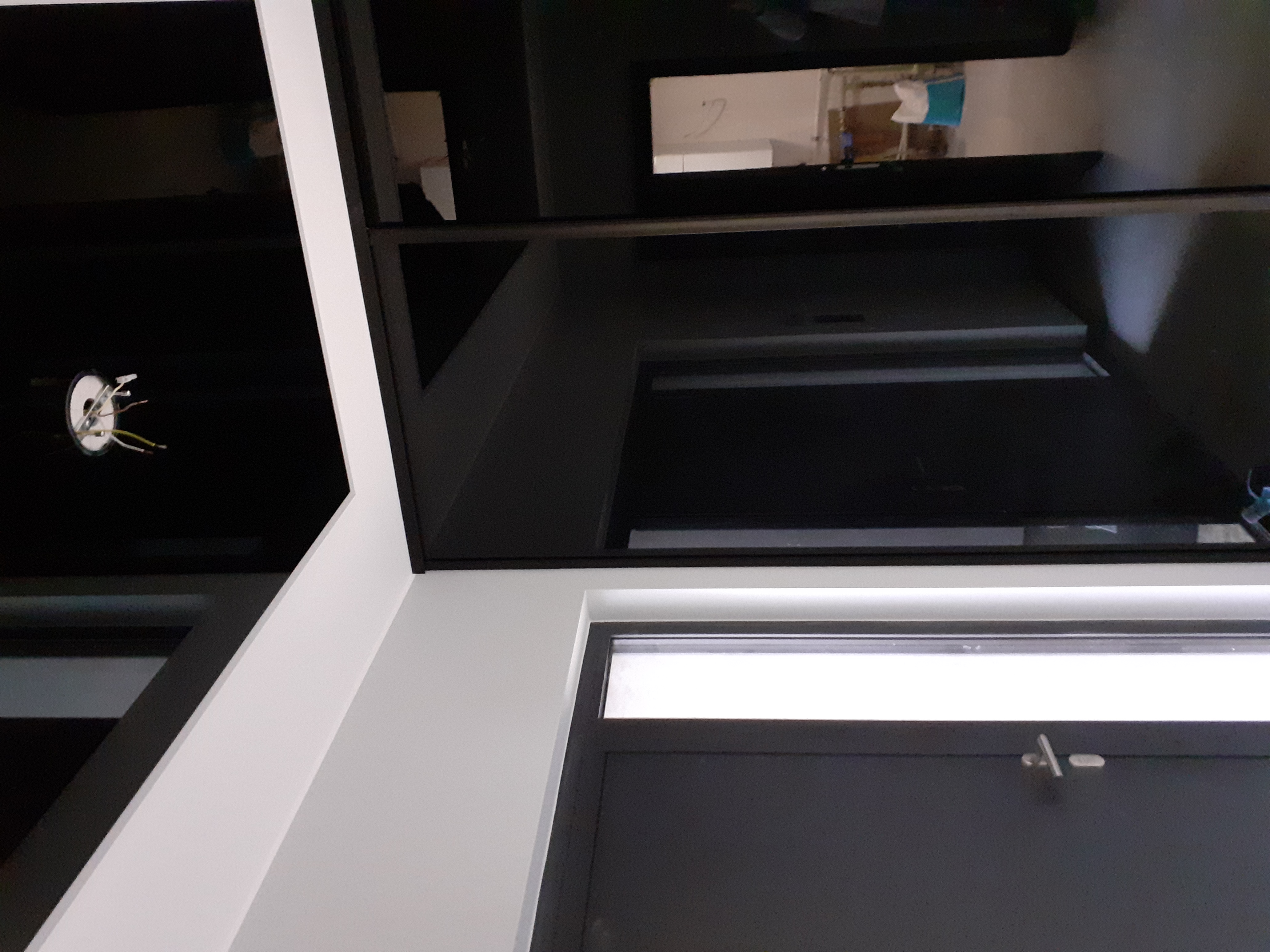 Fragment sufitu z zamontowanym oświetleniem, widoczne przewody, ściana pomalowana na biało, czarne elementy wykończeniowe, drzwi w kolorze grafitowym.