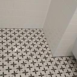 Reformas Generales - Białe płytki ścienne i podłogowe z wzorem czarnych kwiatów w łazience, obok umywalka w folii ochronnej.