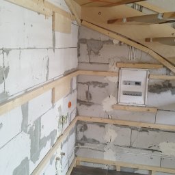 Reformas Generales - Wnętrze w trakcie remontu: białe ściany z betonu komórkowego z widocznymi śladami zaprawy, drewniane listwy mocujące do płyt karton-gips, instalacja elektryczna, skrzynka bezpiecznikowa i fragment...