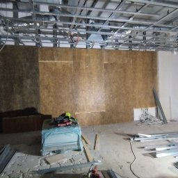 Reformas Generales - Montaż stelaża pod płytę karton gips: widoczna konstrukcja metalowa sufitu podwieszanego, płyty OSB na ścianach, narzędzia i materiały budowlane na podłodze.