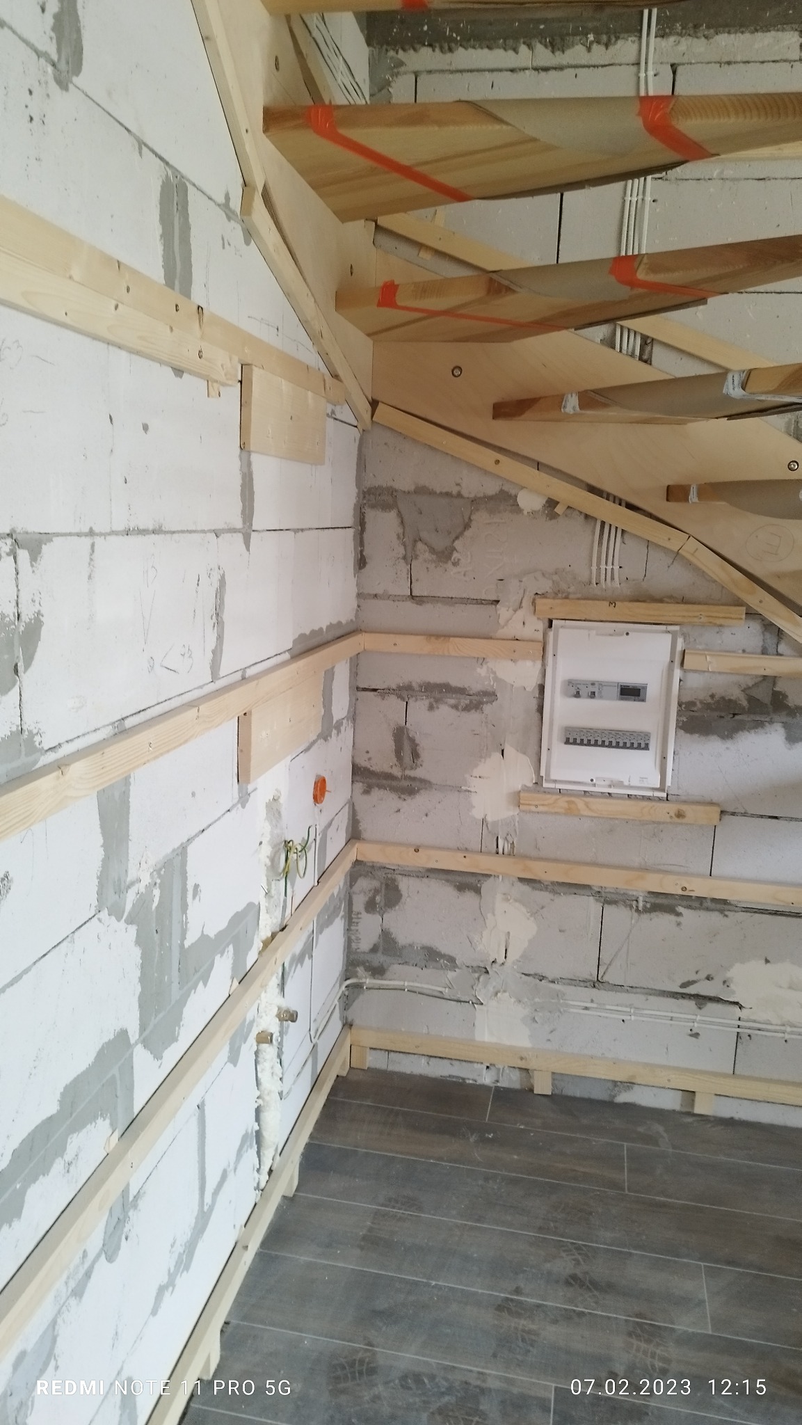 Wnętrze w trakcie remontu: białe ściany z betonu komórkowego z widocznymi śladami zaprawy, drewniane listwy mocujące do płyt karton-gips, instalacja elektryczna, skrzynka bezpiecznikowa i fragment...