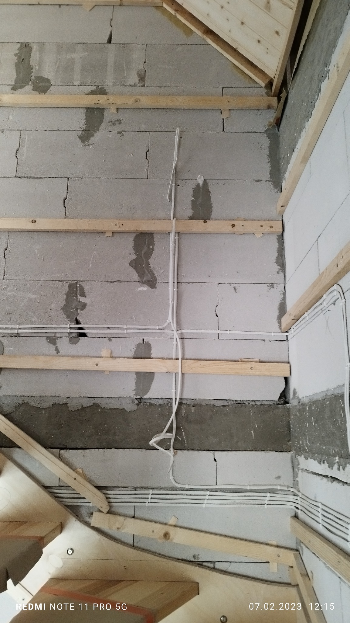 Ściana z betonu komórkowego z widocznymi przewodami elektrycznymi przymocowanymi do drewnianych łat, przygotowana do dalszych prac wykończeniowych, widoczne fragmenty drewnianej konstrukcji dachu...
