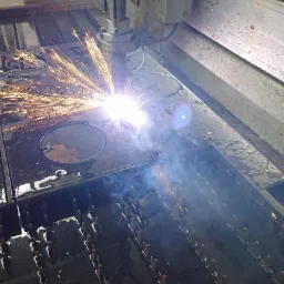 Proces cięcia plazmowego grubej, czarnej blachy z widocznymi iskrami i dymem, tworzący okrągłe otwory.