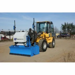 Żółta niwelarka Volvo z niebieskim ostrzem profilującym 'Profiler 01' na piaszczystym placu budowy, widoczne drzewa i ogrodzenie w tle.