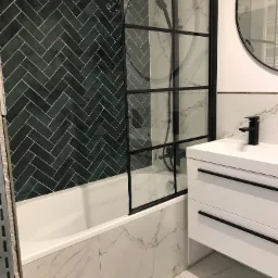 Wykończona łazienka w Gdańsku: ciemnozielona ściana z płytek ułożonych w jodełkę, biała wanna z czarną kabiną prysznicową, umywalka z szafką i czarną baterią oraz okrągłe lustro.