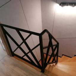 Luk.steel Łukasz Bogdański zpuh - Nowoczesna, czarna balustrada schodowa z geometrycznym wzorem na drewnianych schodach, oświetlona lampą sufitową
