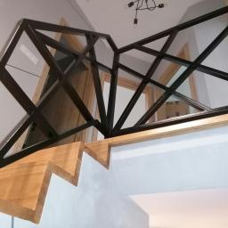 Luk.steel Łukasz Bogdański zpuh - Czarna, geometryczna konstrukcja zabezpieczająca schody z jasnego drewna, widok z dołu, nowoczesne wnętrze.