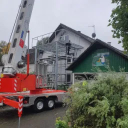 Montaż metalowej konstrukcji balkonu przy domu w Namysłowie, widoczny podnośnik koszowy i pracownik na rusztowaniu.