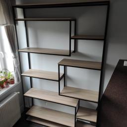 Luk.steel Łukasz Bogdański zpuh - Regał metalowy z drewnianymi półkami w stylu industrialnym, ustawiony przy białej ścianie, widoczne rośliny doniczkowe na parapecie obok okna.