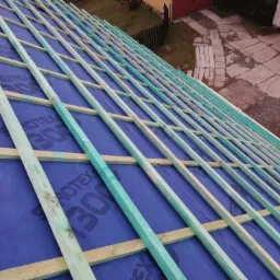 Konstrukcja drewniana dachu pokryta niebieską membraną dachową, widok z góry na szkielet dachu przed położeniem pokrycia.