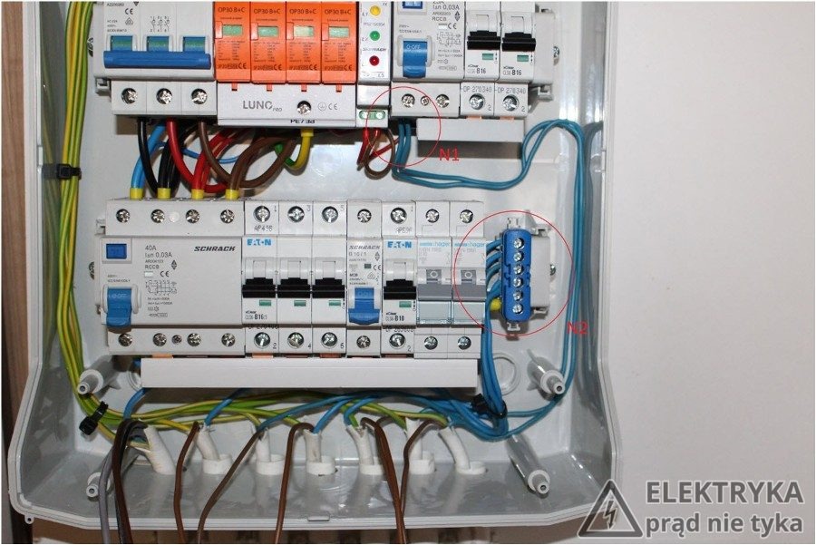 Otwarta skrzynka elektryczna z zabezpieczeniami różnicowoprądowymi, bezpiecznikami i listwami zaciskowymi, widoczne okablowanie w różnych kolorach.