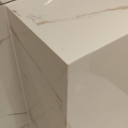 Expert Build - Biała umywalka nablatowa z marmurowym wzorem, ostra krawędź blatu, odbicie światła na powierzchni.