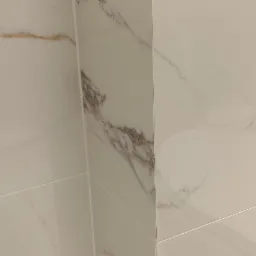 Detal narożnika wykończonego białymi, połyskującymi płytkami imitującymi marmur z szarymi i złotymi żyłkami.