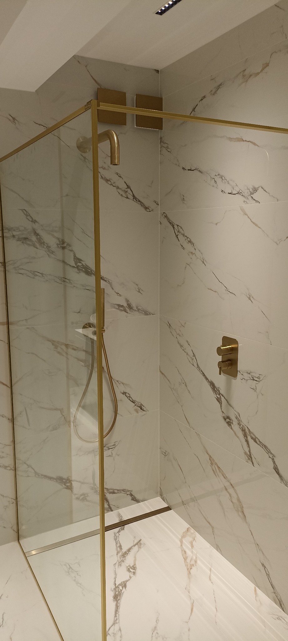 Kabina prysznicowa z marmurowymi płytkami, złotymi okuciami i deszczownicą, nowoczesny design.