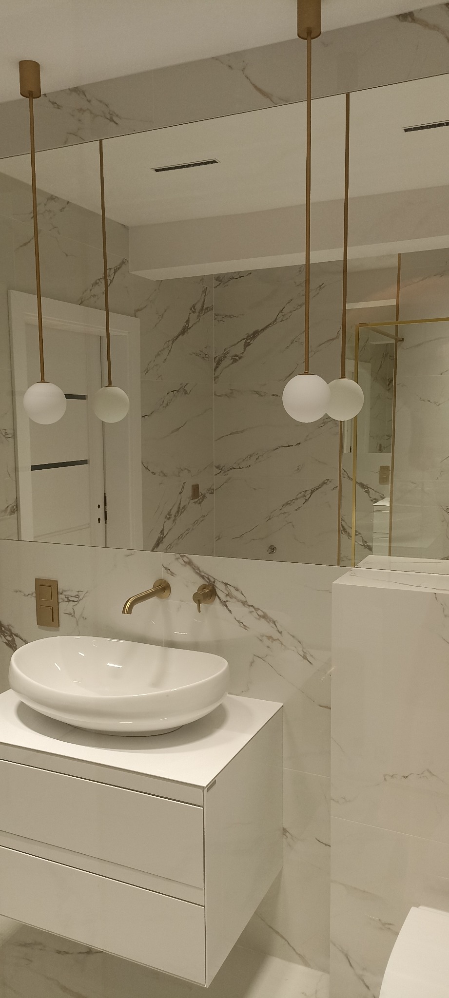 Nowoczesna łazienka z umywalką nablatową, złotą armaturą i marmurowymi płytkami, oświetlona wiszącymi lampami z kulistymi kloszami.