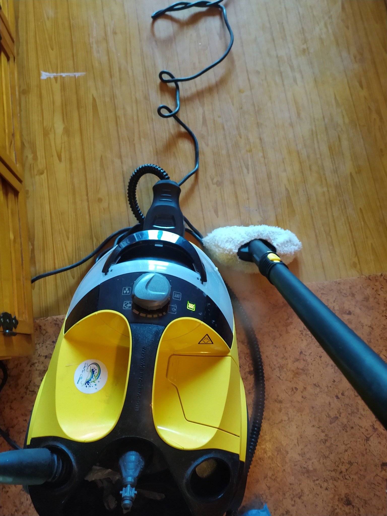 Żółto-czarny parownica Karcher z naklejką firmy w trakcie użycia na drewnianej podłodze, widoczna para.