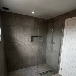 Home fix studio łazienki - Nowoczesna łazienka z kabiną typu walk-in, wykończona szarymi płytkami w różnych odcieniach i wzorach. Widoczny odpływ liniowy i wnęka w ścianie.