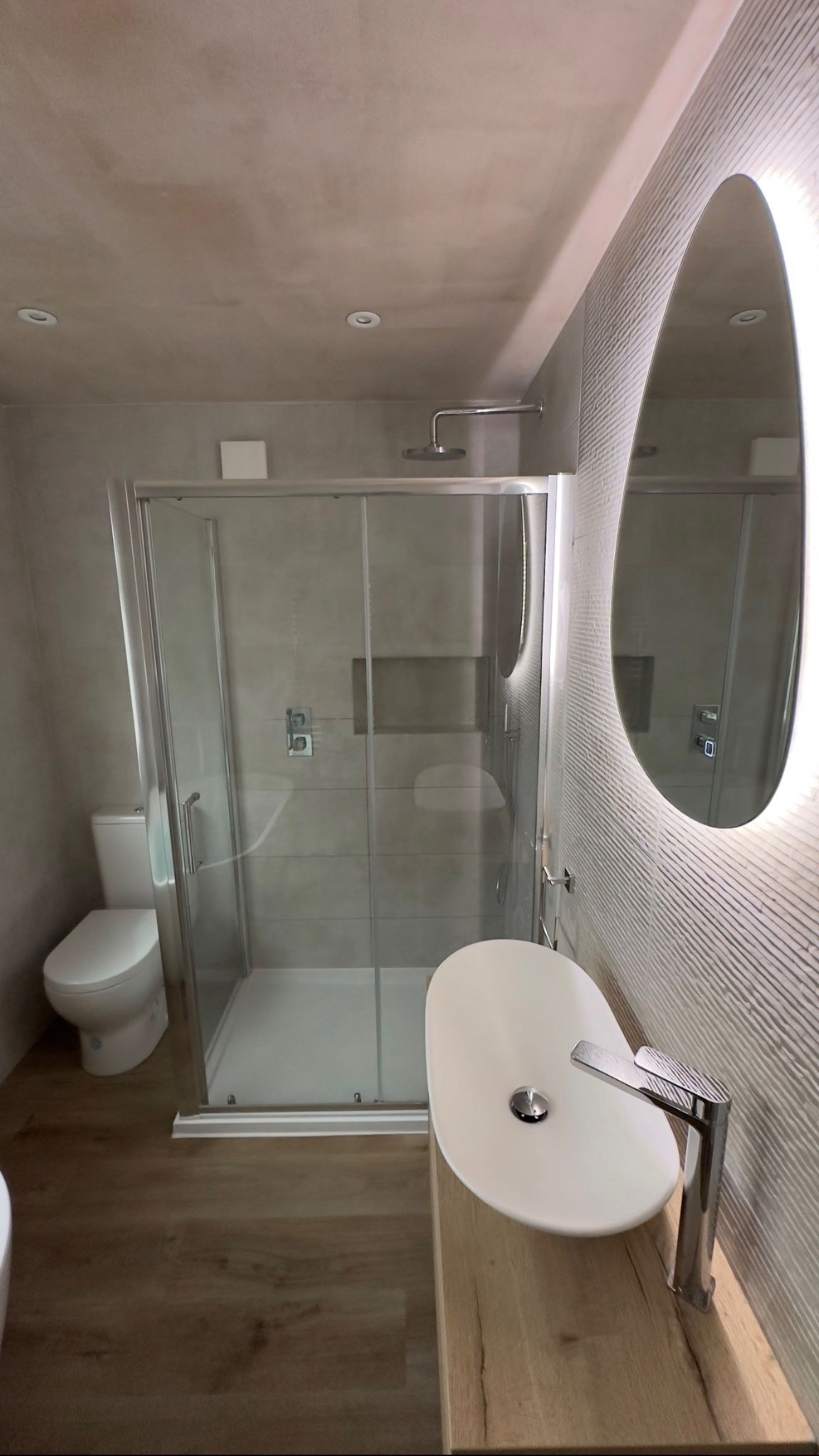 Nowoczesna łazienka po remoncie w Świdnicy: kabina prysznicowa ze szklanymi drzwiami, umywalka nablatowa na drewnianym blacie, podświetlane lustro owalne i płytki imitujące drewno.