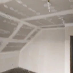 Poddasze z ukończonym montażem płyt kartonowo-gipsowych na ścianach i skosach sufitu, widoczne łączenia płyt przed szpachlowaniem, kabel zwisający z sufitu.