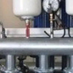 Metalowa instalacja przemysłowa z trzema białymi zbiornikami i manometrem, widoczne spawane łączenia rur.