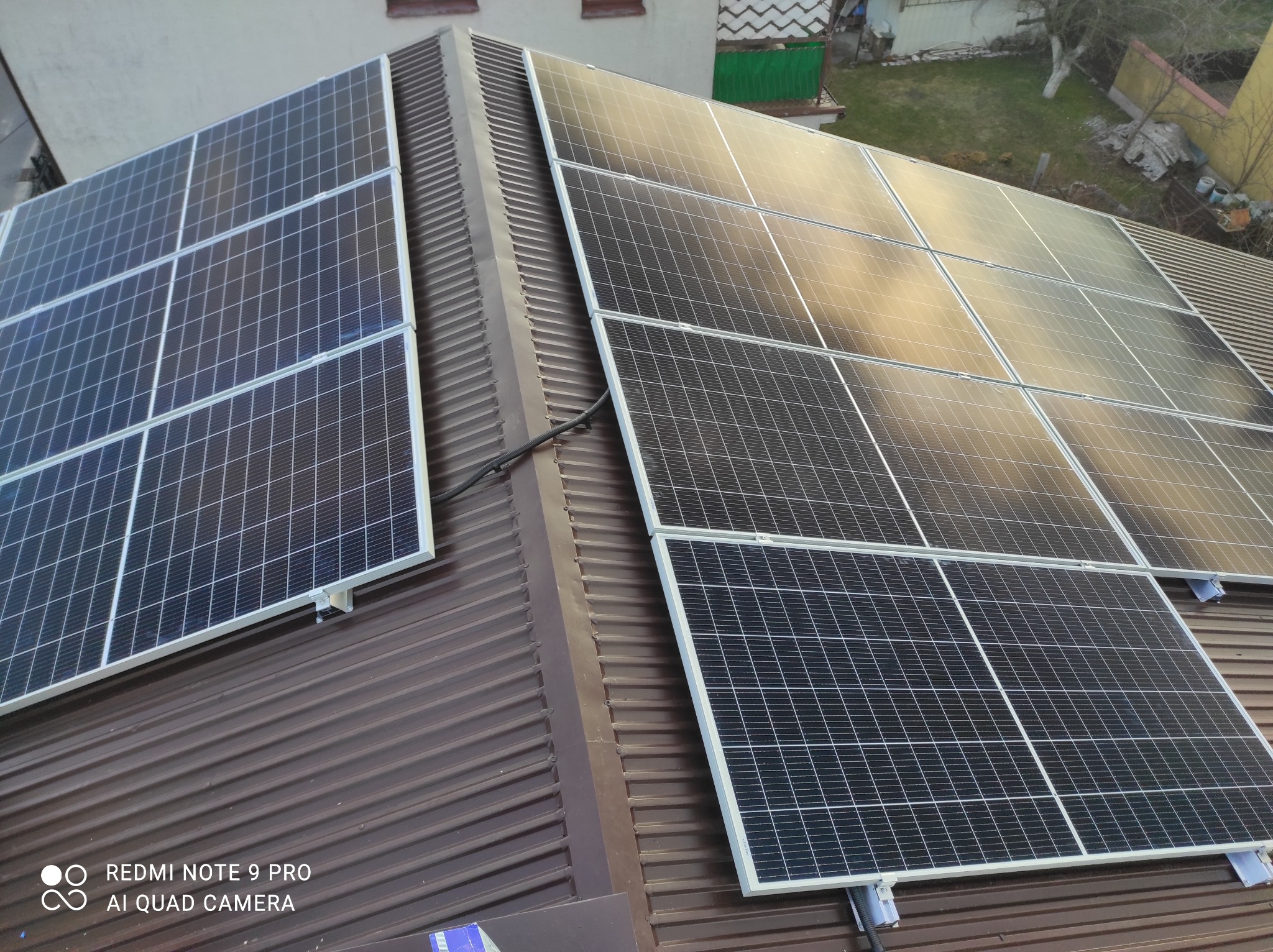 Panele słoneczne zamontowane na brązowym, blaszanym dachu domu jednorodzinnego, widok z góry.