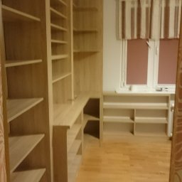 BBud - Jasne, drewniane regały z półkami, zabudowa narożna z blatem biurka, widok na okno z zasłonami w paski, parkiet na podłodze.